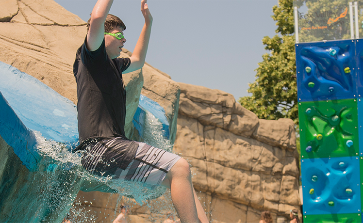 Teen boy wearing green goggles coming out of water slide